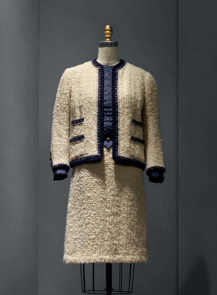 INew York Calling: House of Chanel, 1963-68, Haute Couture Suit: machine-sewn ivory wool bouclé tweed, hand-applied navy and ivory wool knit trim hand-braided with interlocking chain stitch; blouse: machine-sewn silk broadcloth, machine-embroidered with bound pleats, hand-worked buttonholes.